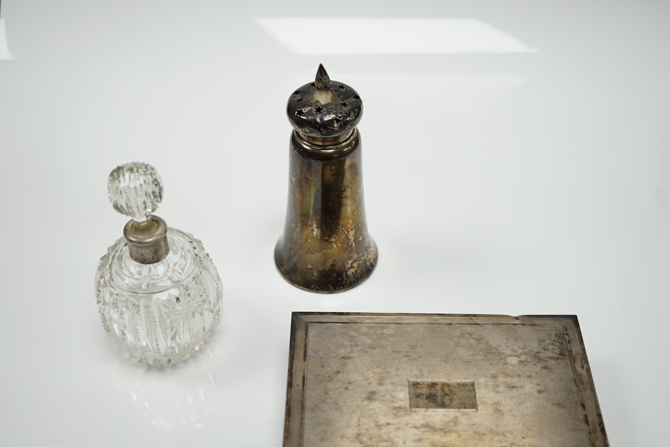 A 1970's engine turned silver mounted rectangular cigarette box, a silver mounted glass sugar caster and a similar scent bottle.